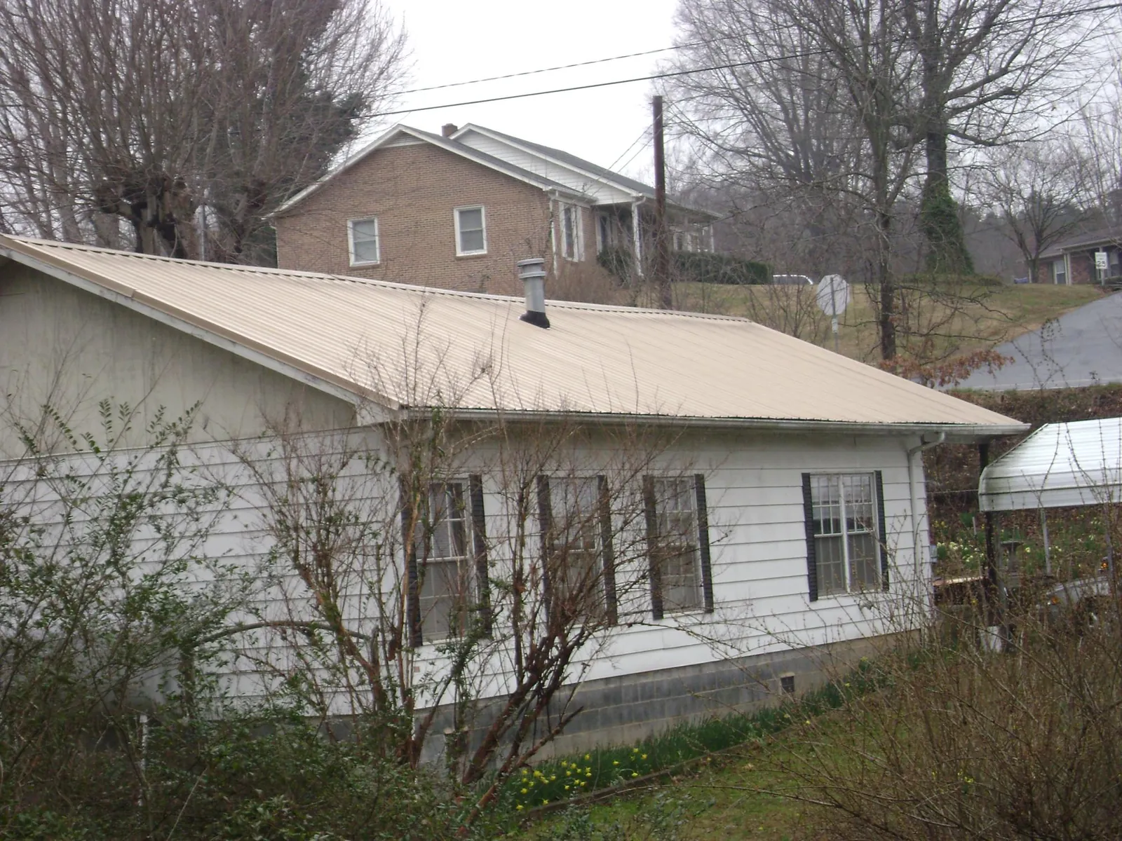 Tan metal roof on a white sided house set into a hillside — Commercial Roofing by Roofing Brothers in Castleton On Hudson